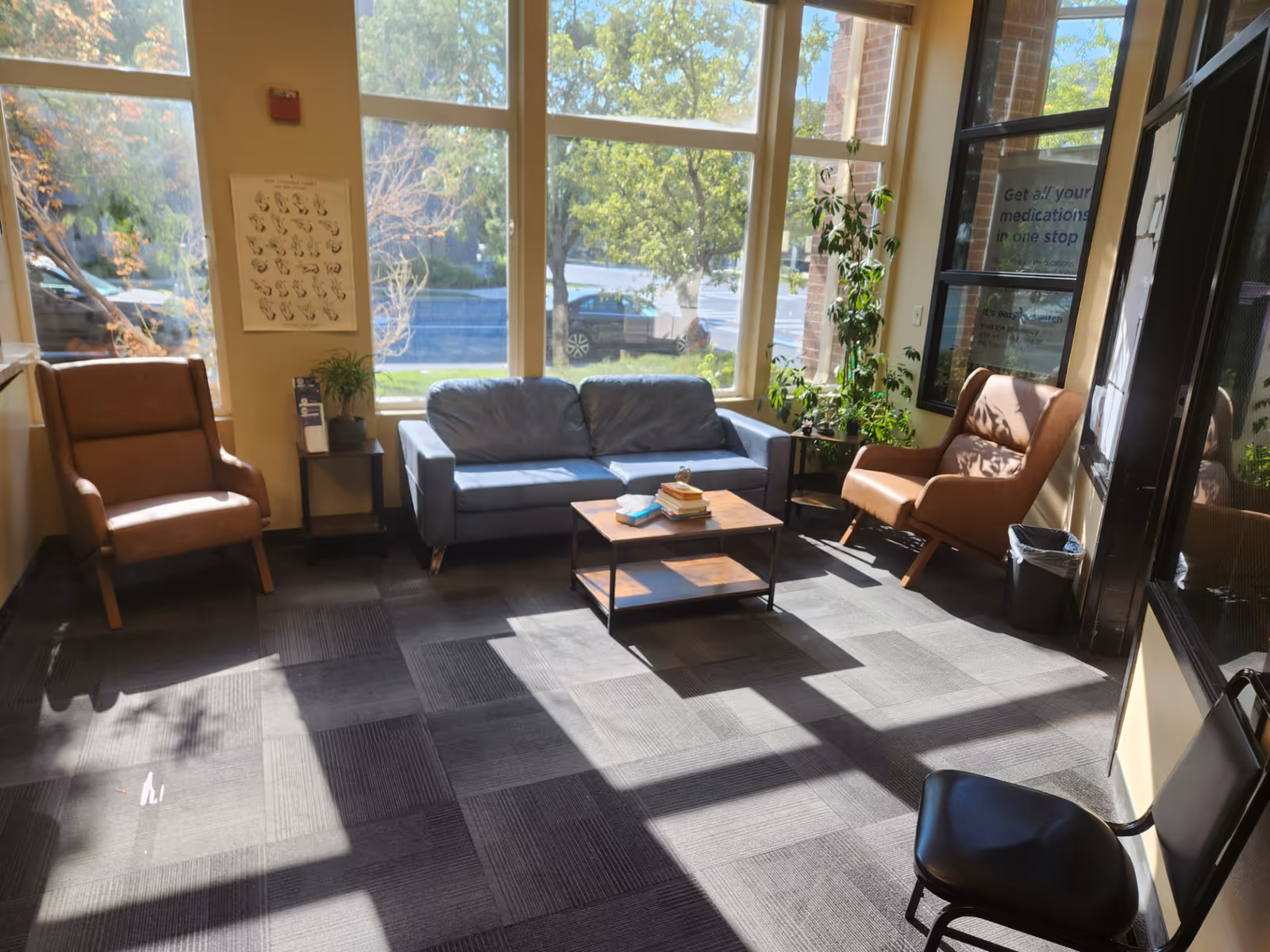 Sunlit waiting area with sofa, armchairs, coffee table, and potted plants.