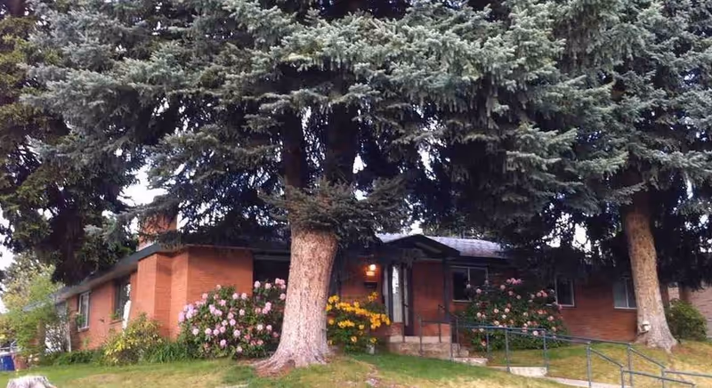 Brick senior living home with trees, flowers, and a welcoming entrance.