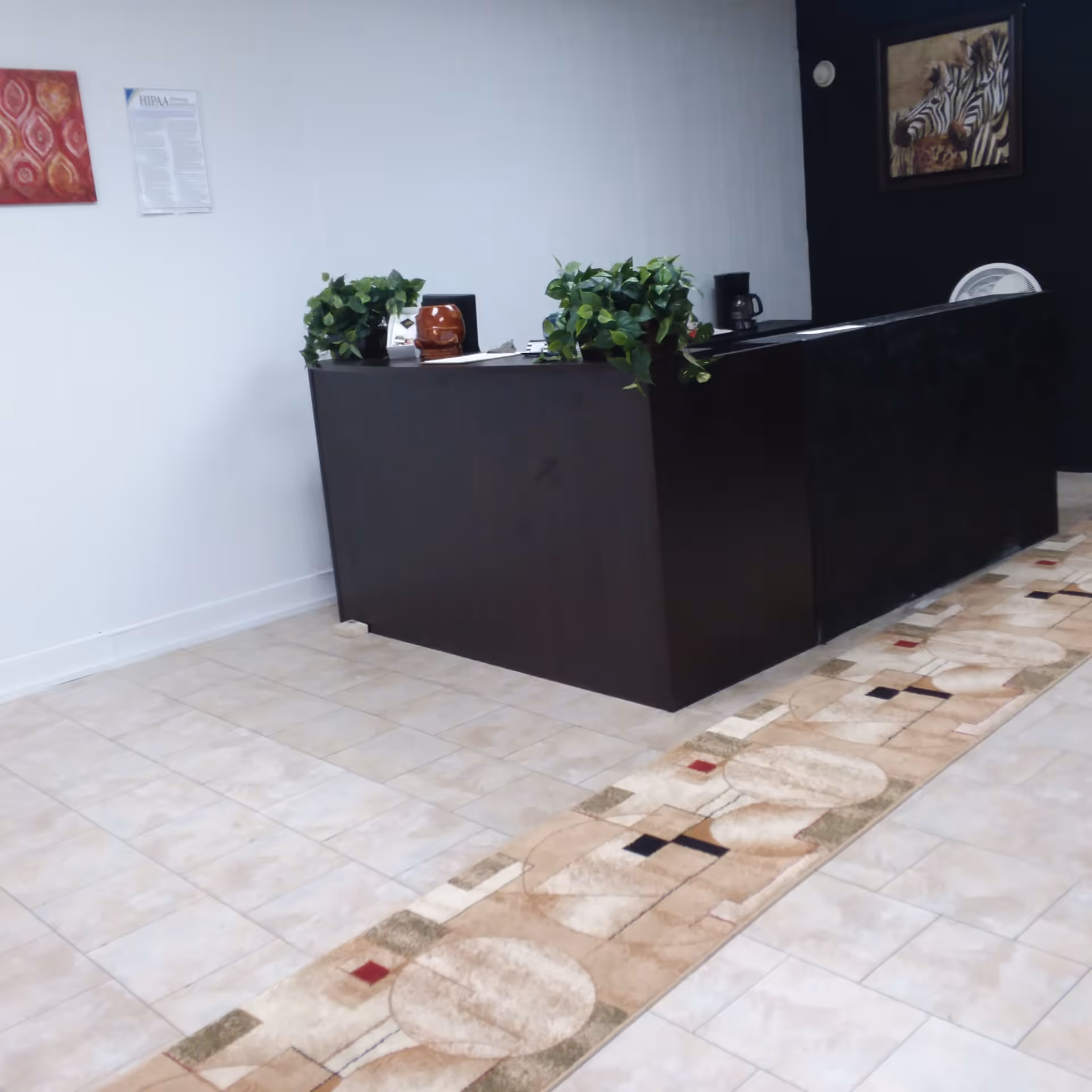 Black reception desk in a lobby with plants, wall art, and a patterned floor runner.