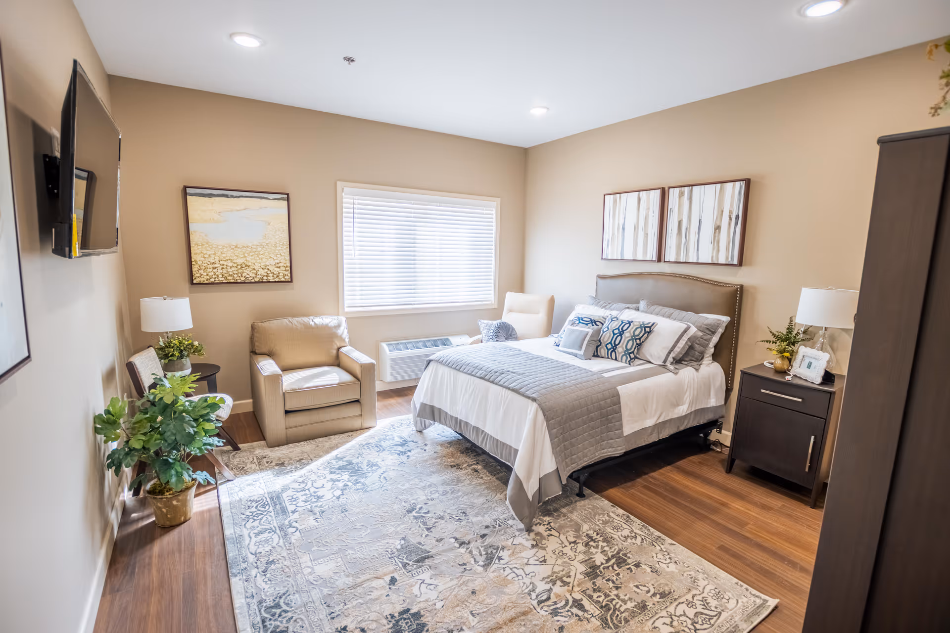 A modern, softly lit bedroom in a senior living facility with bed and seating.
