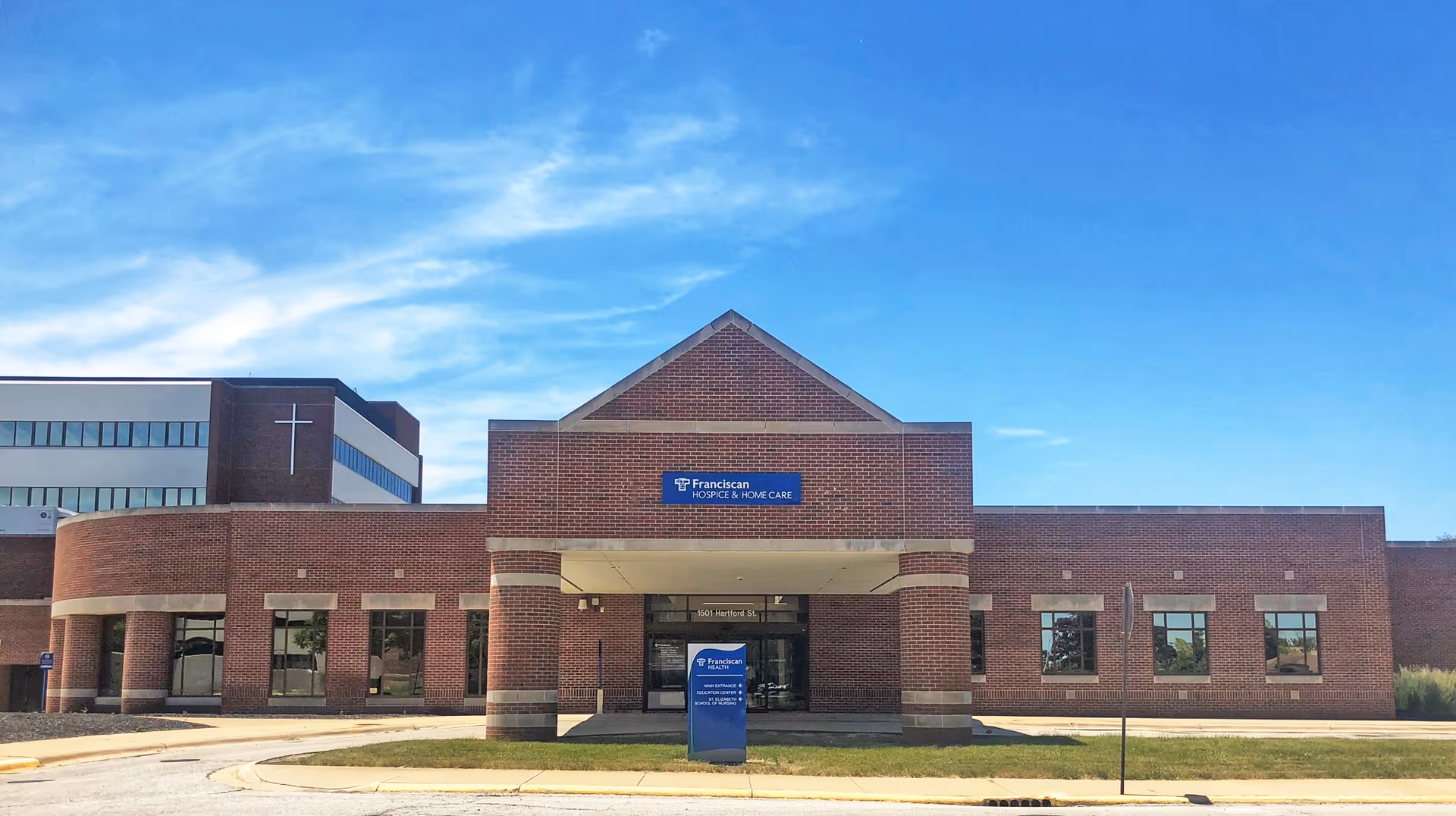 Brick building exterior of Franciscan Hospice & Home Care with a blue entrance sign.