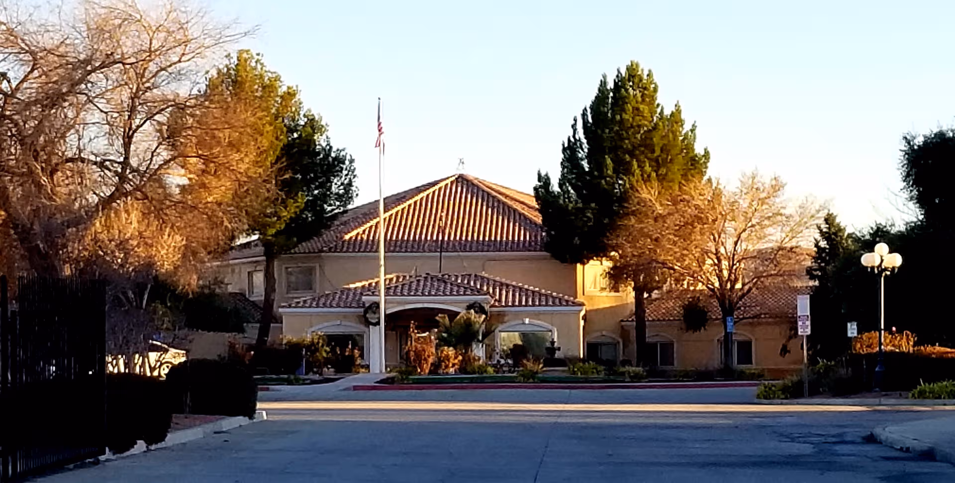 Exterior view of a beige senior living facility with a tiled roof and flagpole.