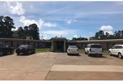 Exterior view of a single-story nursing facility with a covered entrance and parked cars.