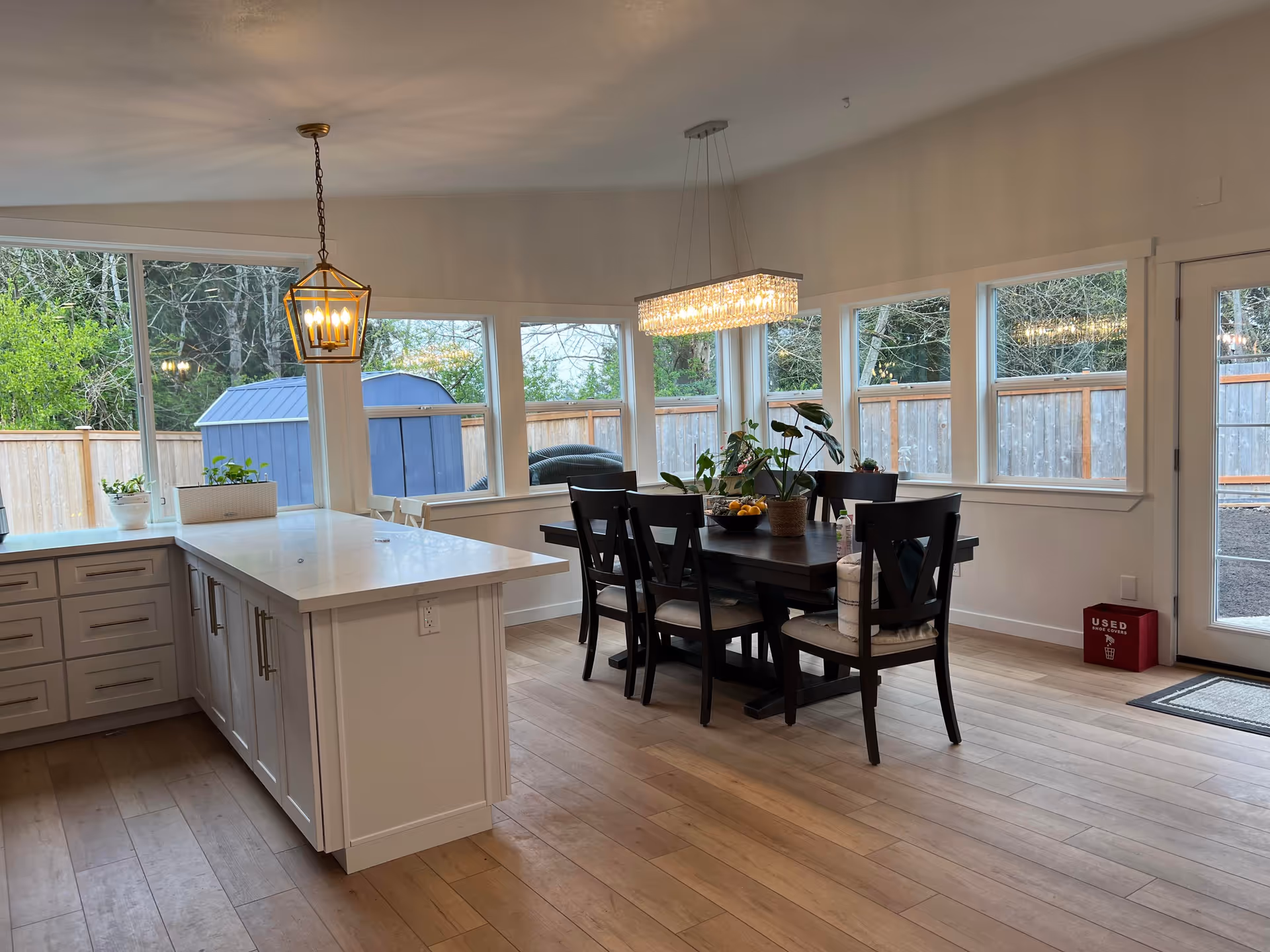 Bright open dining room with dark wood table, chairs, chandelier, kitchen island, and large windows.