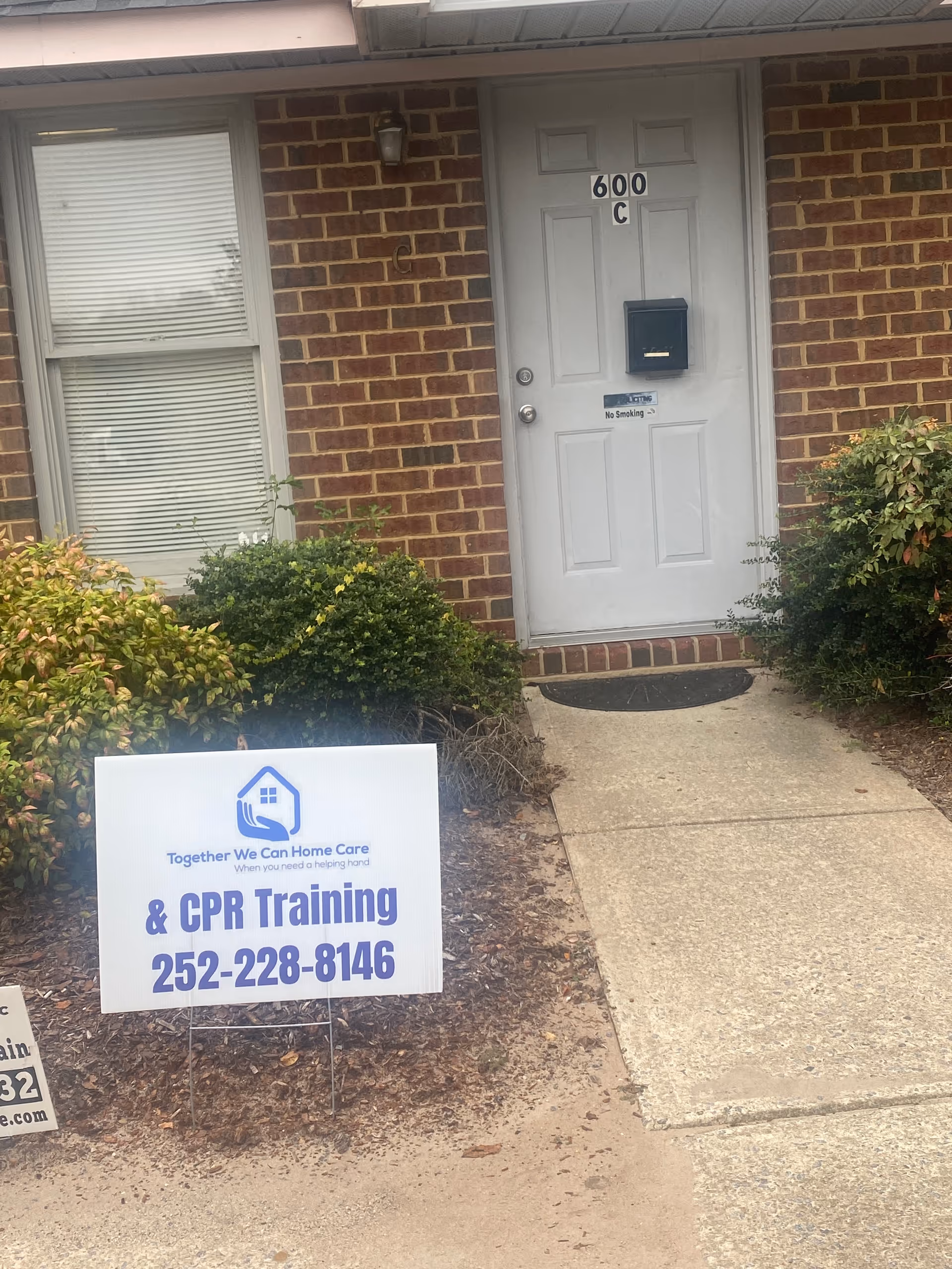 Brick exterior with white door, greenery, and a sign advertising CPR training.
