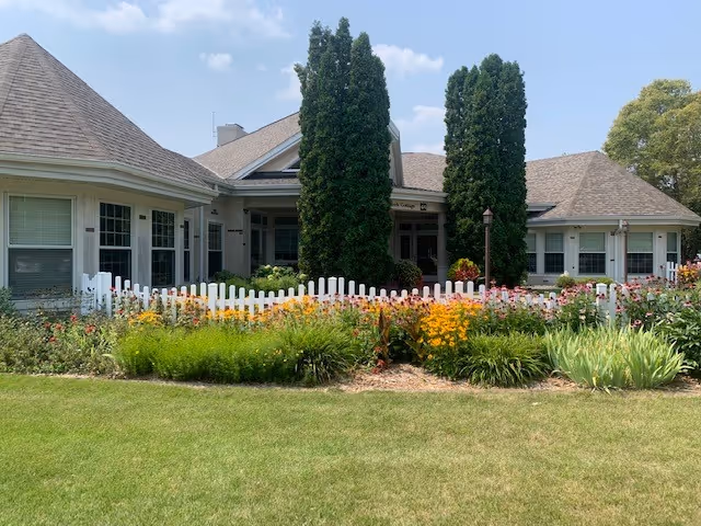 Senior living facility exterior with a white picket fence and vibrant flower garden.