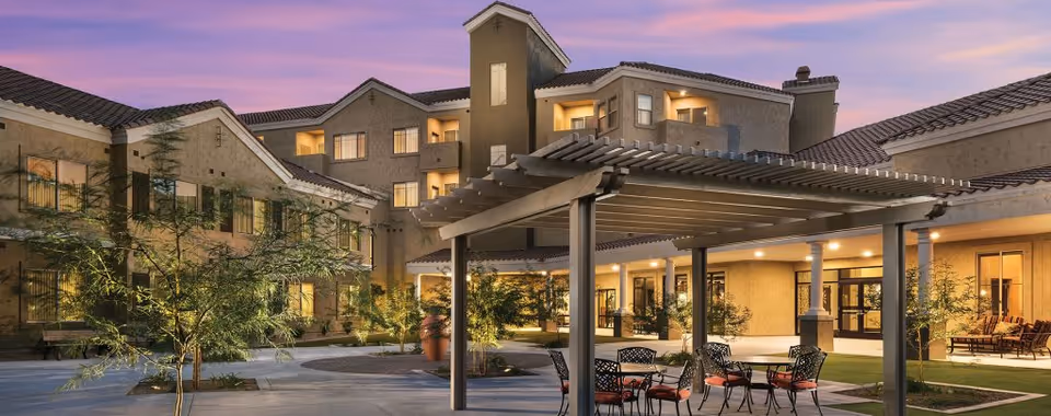 Dusk view of Robson Reserve courtyard showing a pergola with tables and chairs, landscaped walkways, and a lit multi-story building.