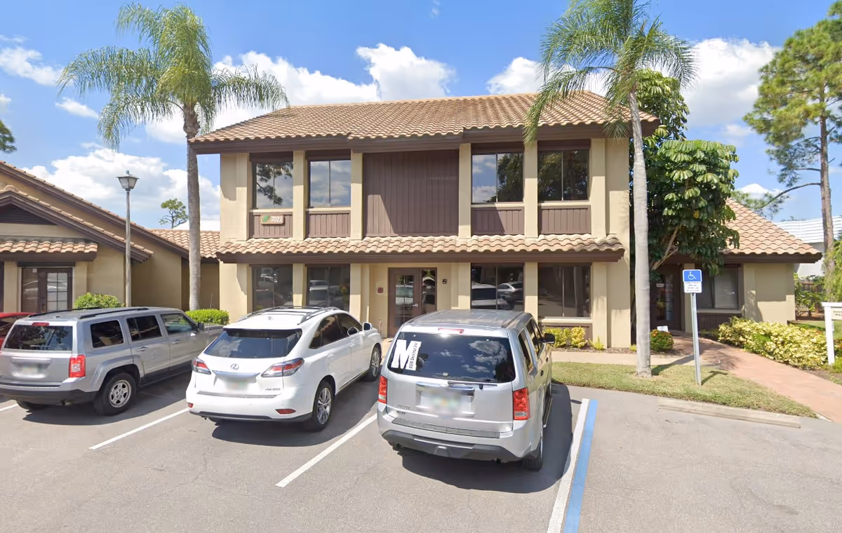 Two-story beige senior housing building with palm trees and parked cars in front.