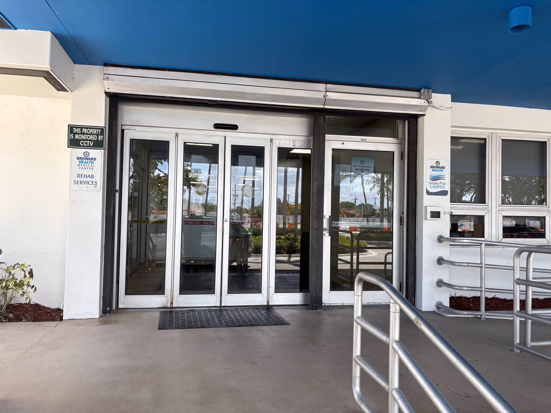 Front entrance with glass double doors, metal rails, and accessibility ramp.