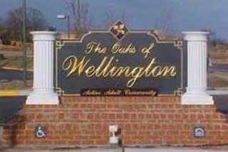 Entrance sign reading The Oaks of Wellington with brick base and white columns.
