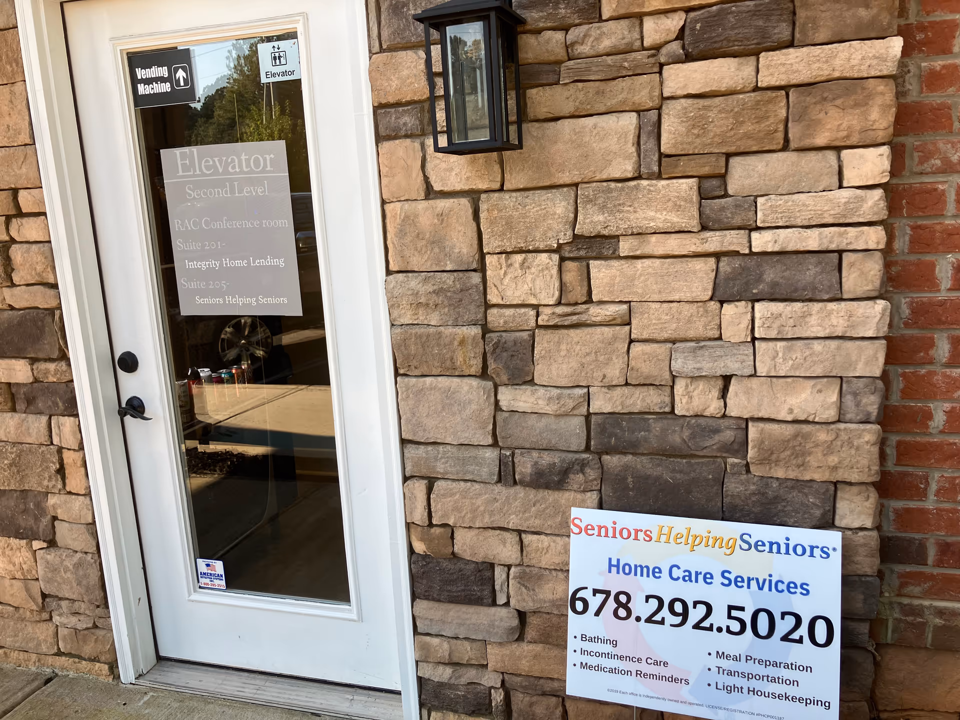 Stone facade with glass door, elevator sign, and a Seniors Helping Seniors home care sign.