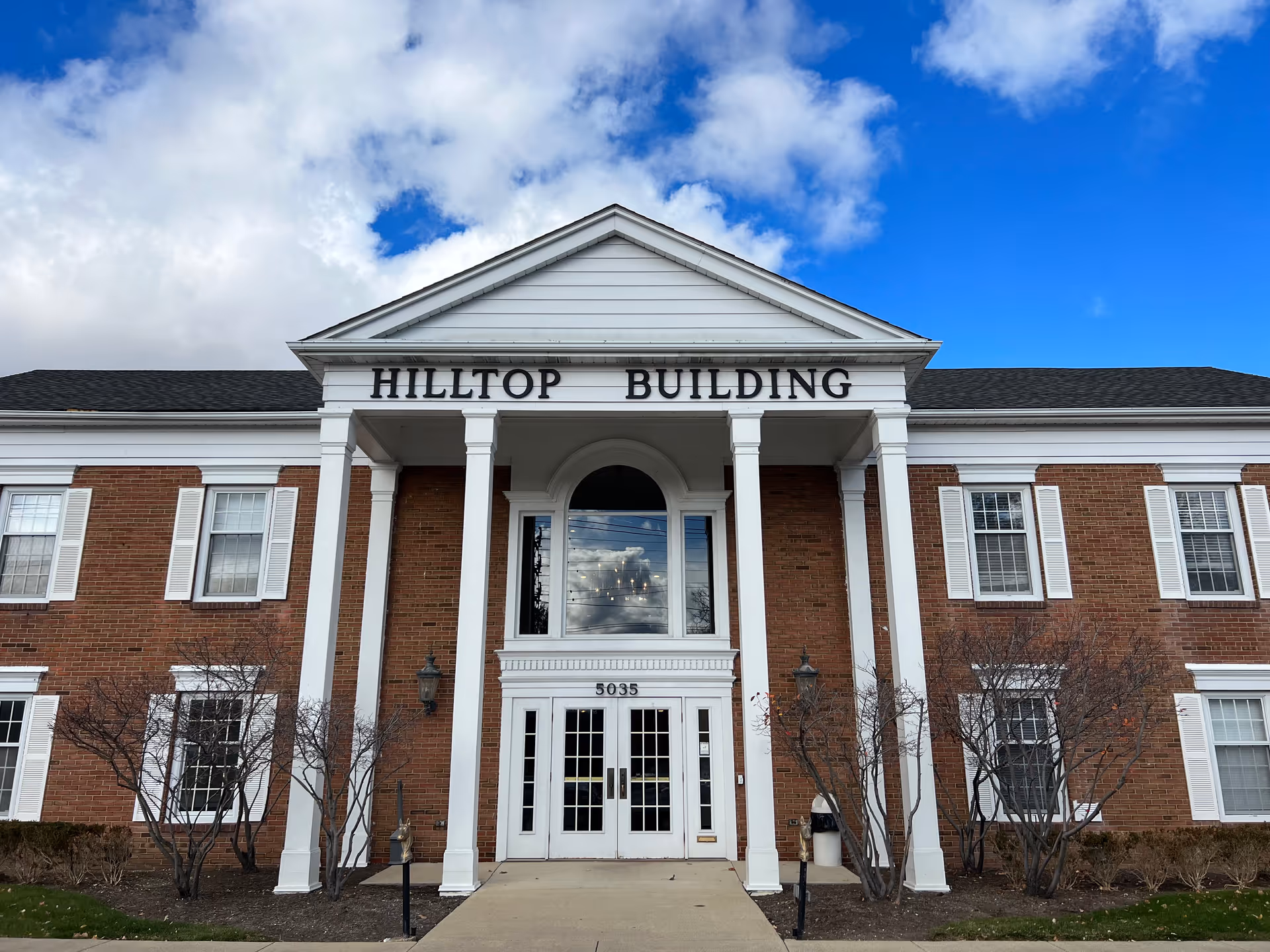 Front facade of Hilltop Building with white columns and brick walls.