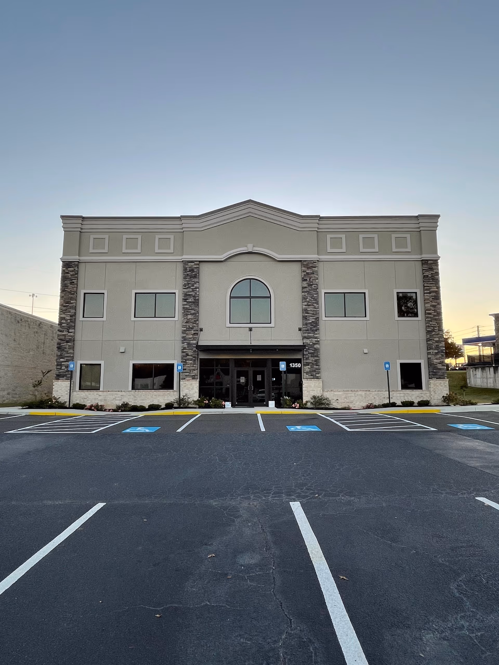 Front view of a two-story building with central arched window and surrounding parking.