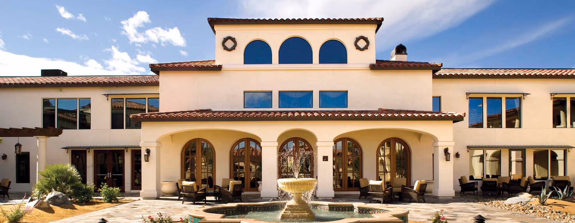 Cream-colored senior living facility with arches, windows, and a central fountain courtyard.