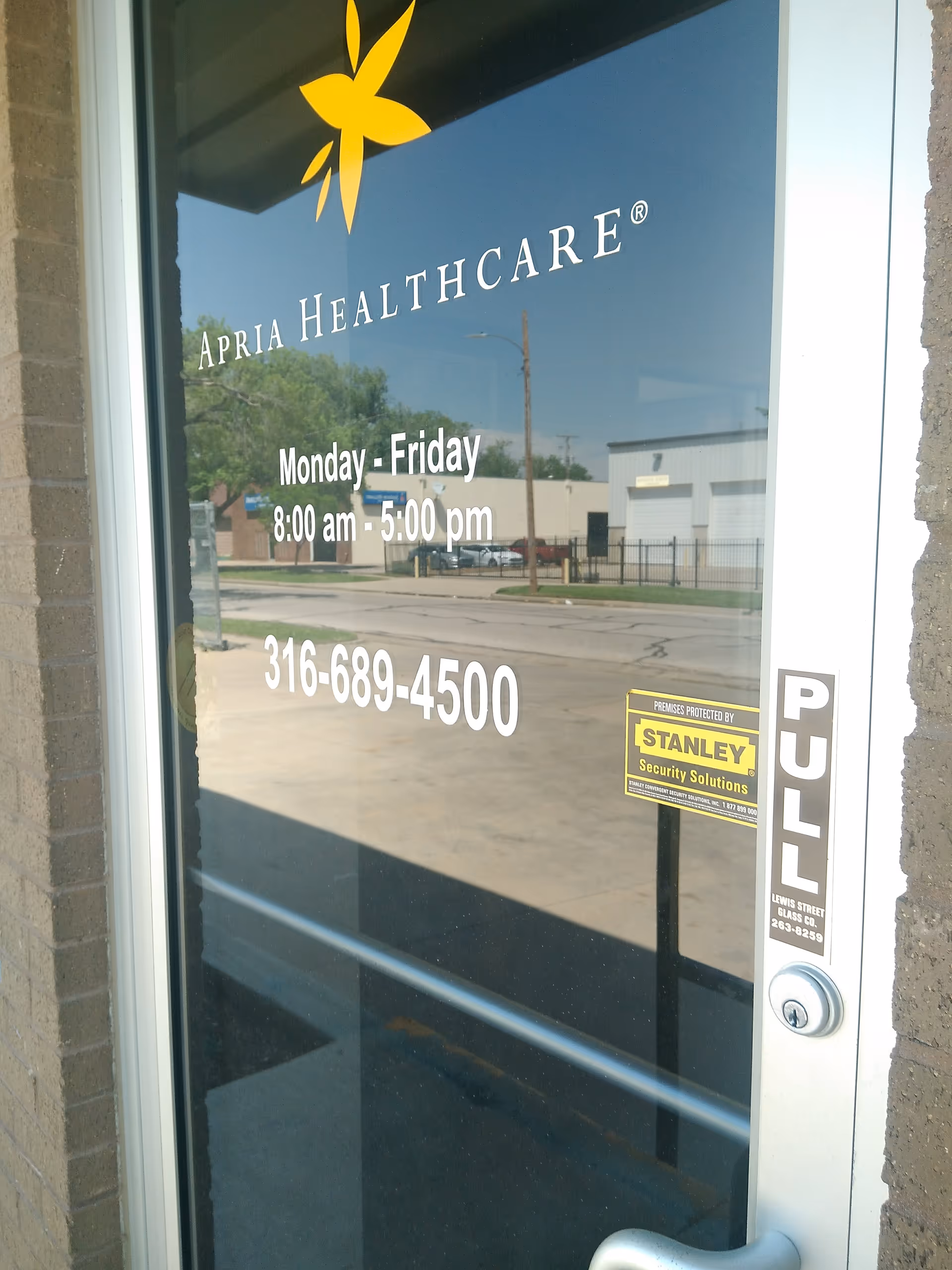 Glass entrance door shows Apria Healthcare logo, hours and phone number.
