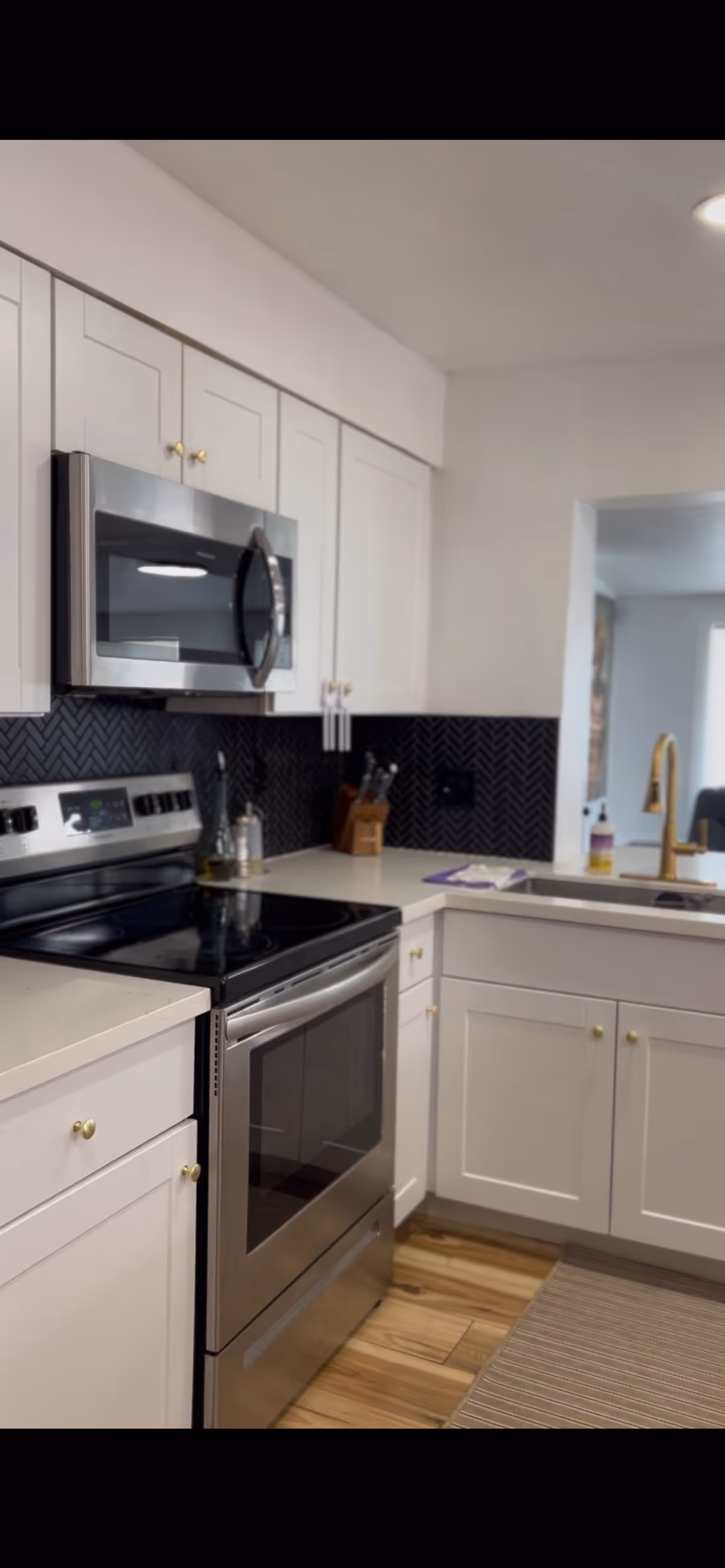 White cabinets, stainless steel appliances, black backsplash, and a sink in a modern kitchen.