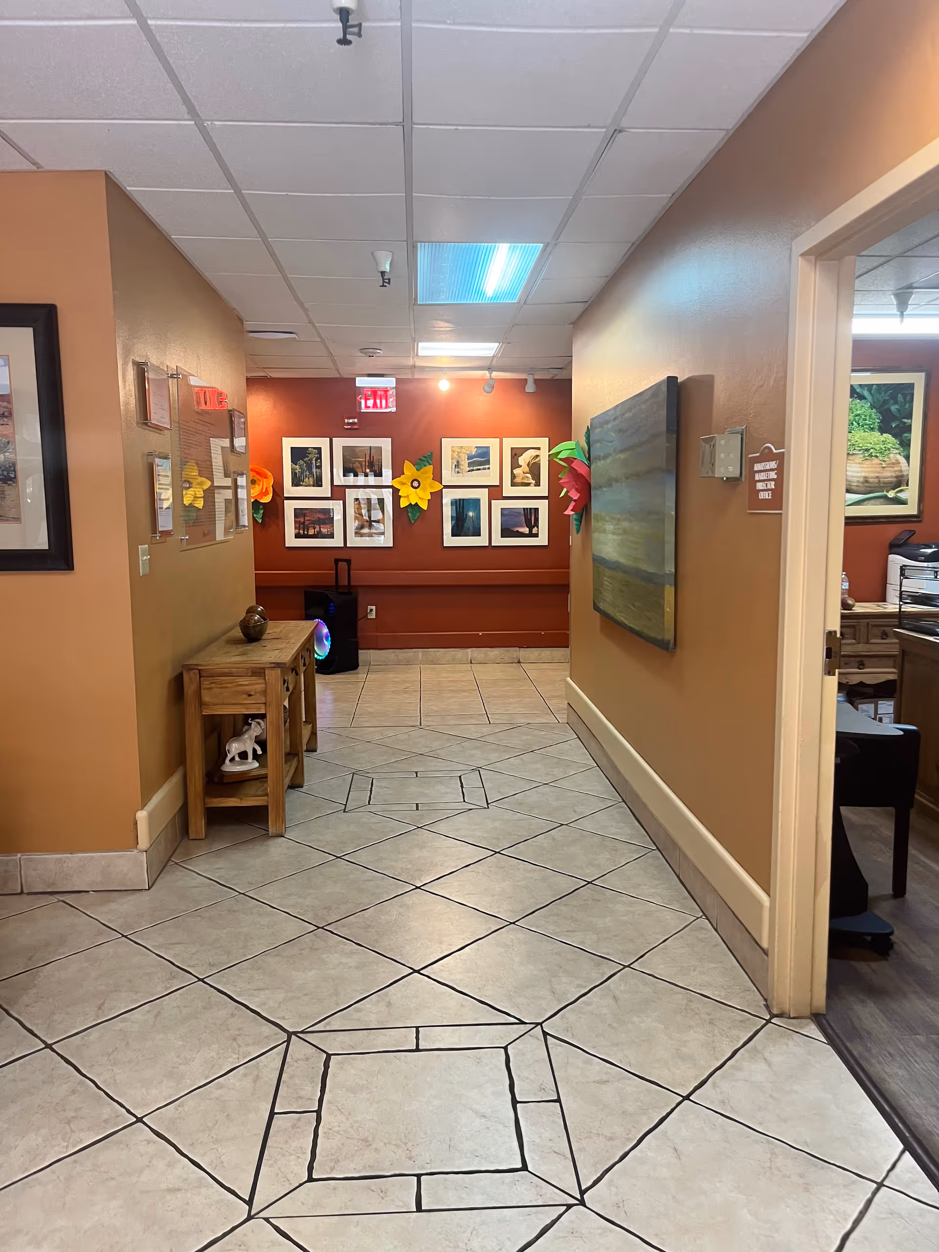 A hallway in a senior living facility with art on walls and tiled floor.