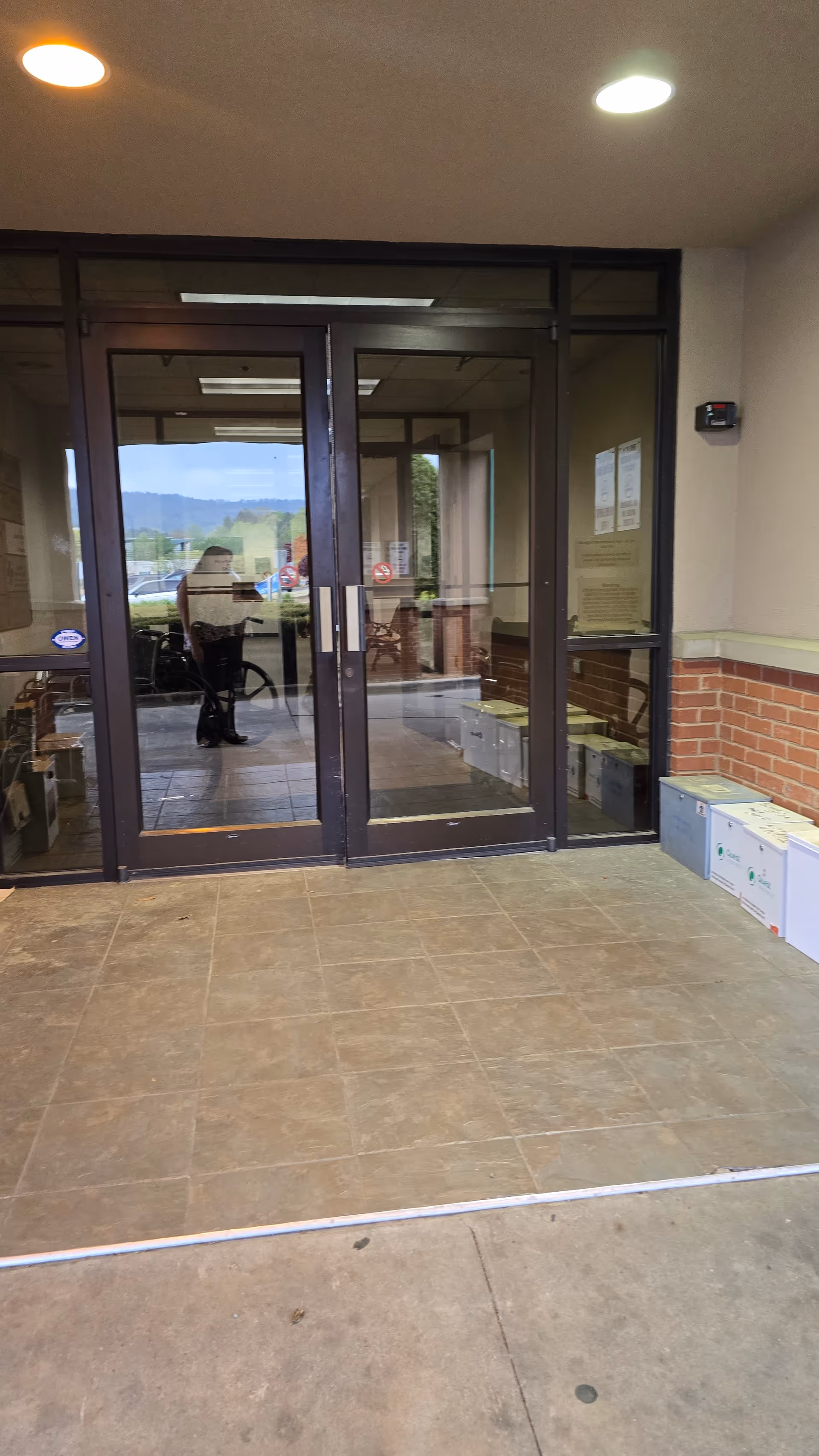 Glass front entrance with double doors, tiled floor, and brick walls.
