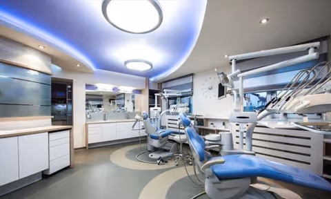 Modern dental clinic with blue chairs, white cabinets, and advanced equipment.