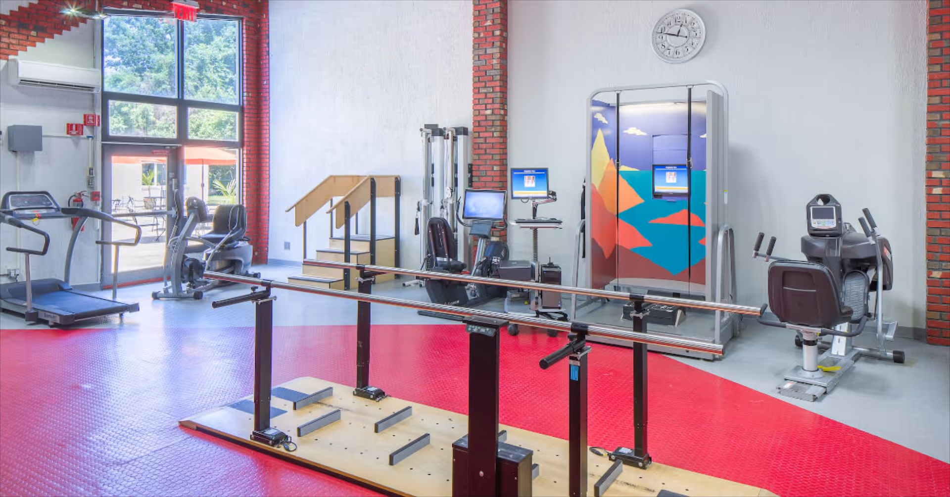 Bright rehabilitation gym with treadmills, stationary bikes, parallel bars, and exercise equipment.