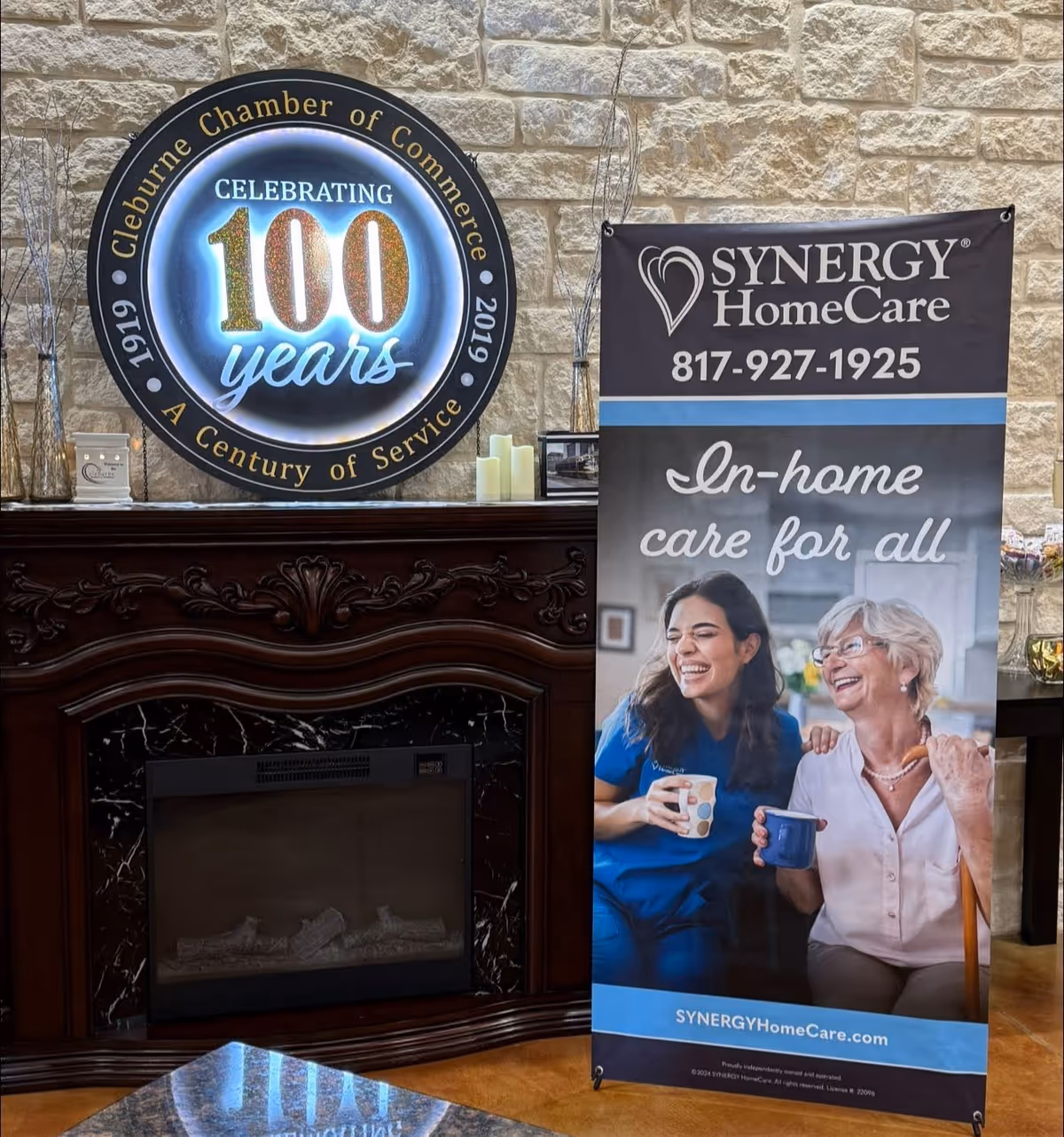 Indoor lobby area with circular 100-year sign and SYNERGY banner beside a stone wall