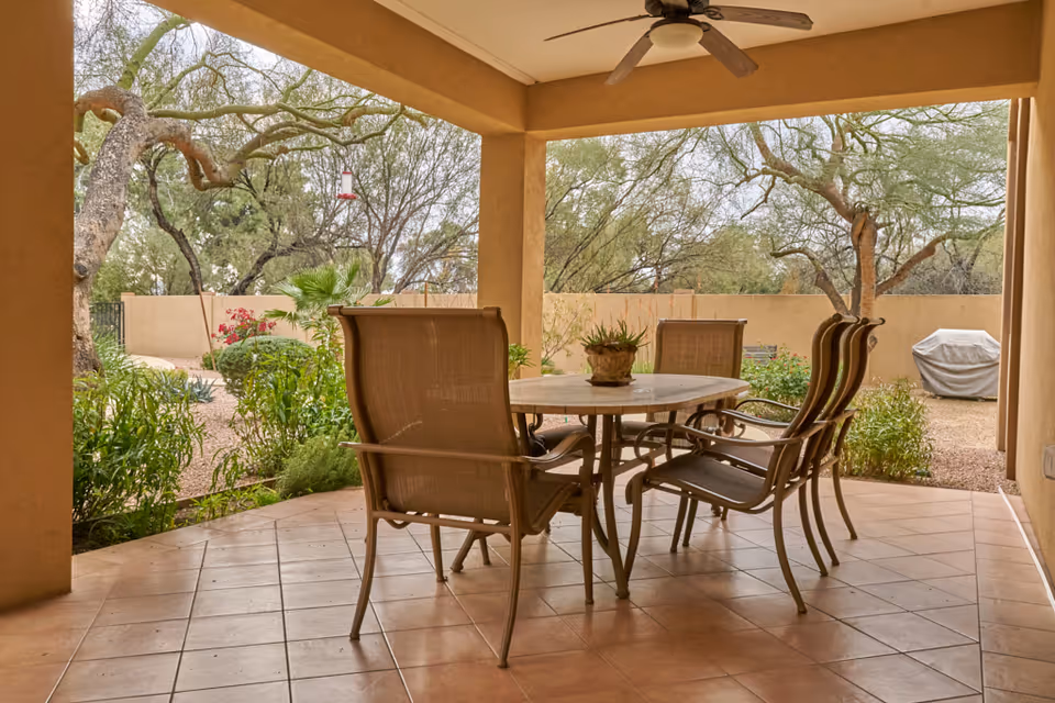 Outdoor covered patio with a round table and several chairs overlooking desert landscaping