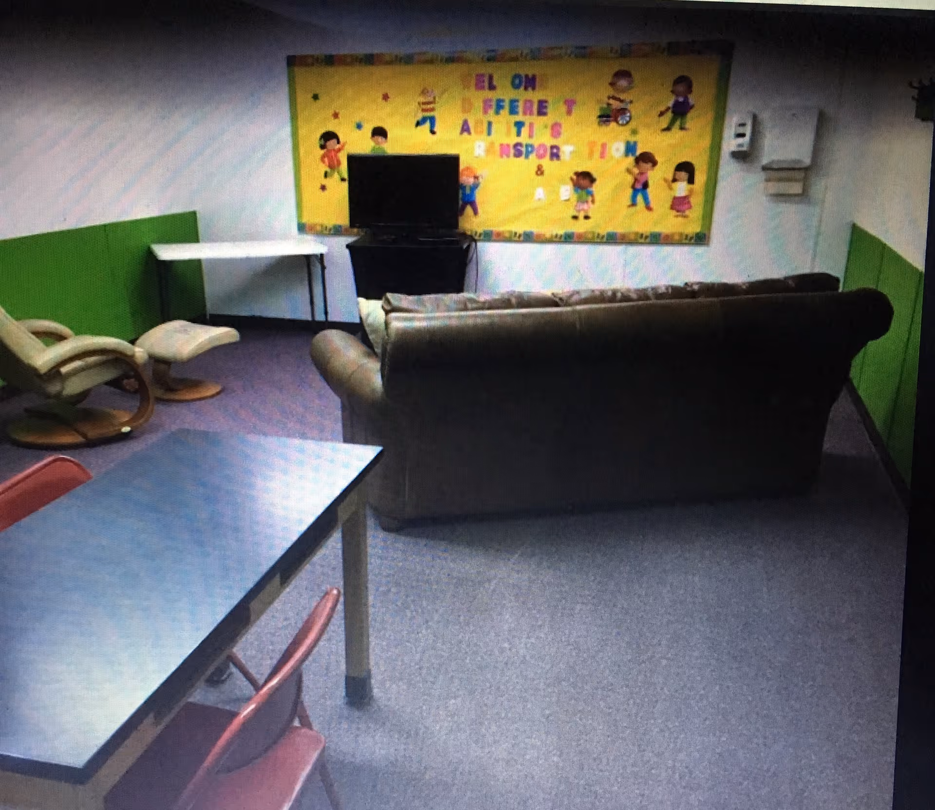 A small indoor living area with a sofa, table, chairs, and a colorful wall poster.