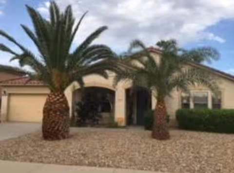Front exterior of an assisted living home with palm trees and desert landscaping.