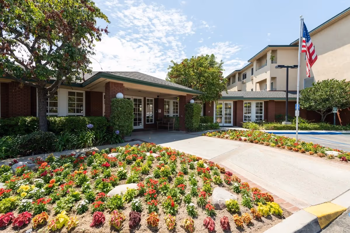 Front entrance of Carmel Village senior living facility with colorful flower beds and landscaping.