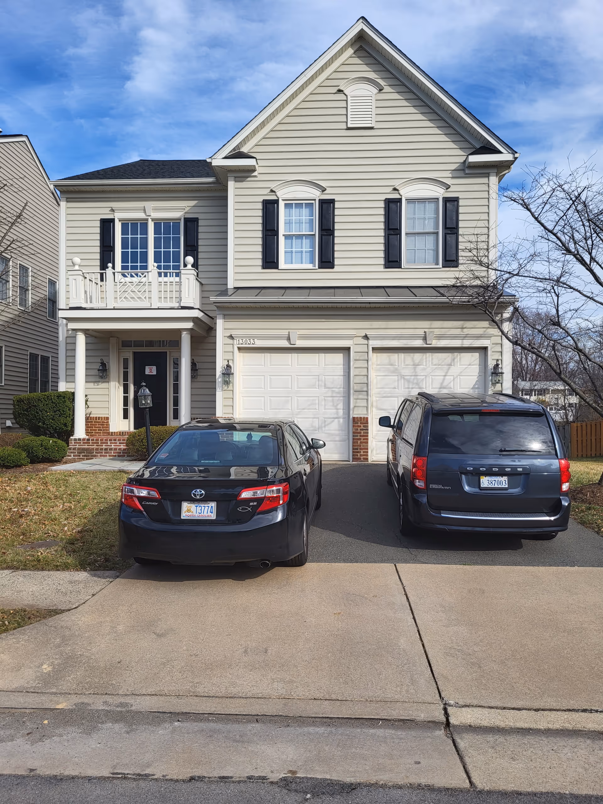 Two-story beige townhouse-style building with two garages and two parked cars in the driveway.