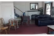 Senior living facility living area with a black sofa, wicker chairs, staircase, and plants.