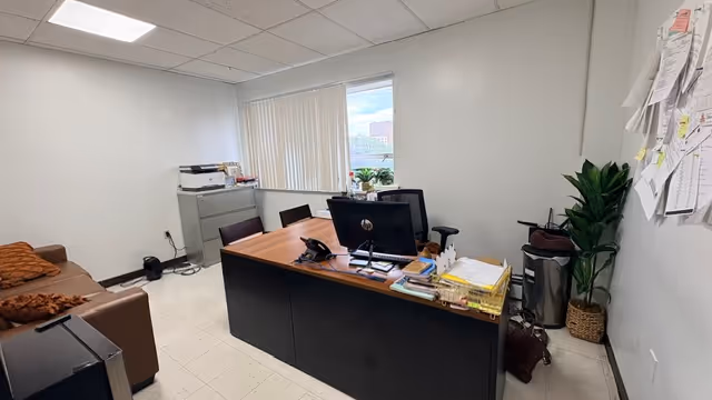 Office desk with dual monitors, paperwork, and plants in a small senior living facility workspace.