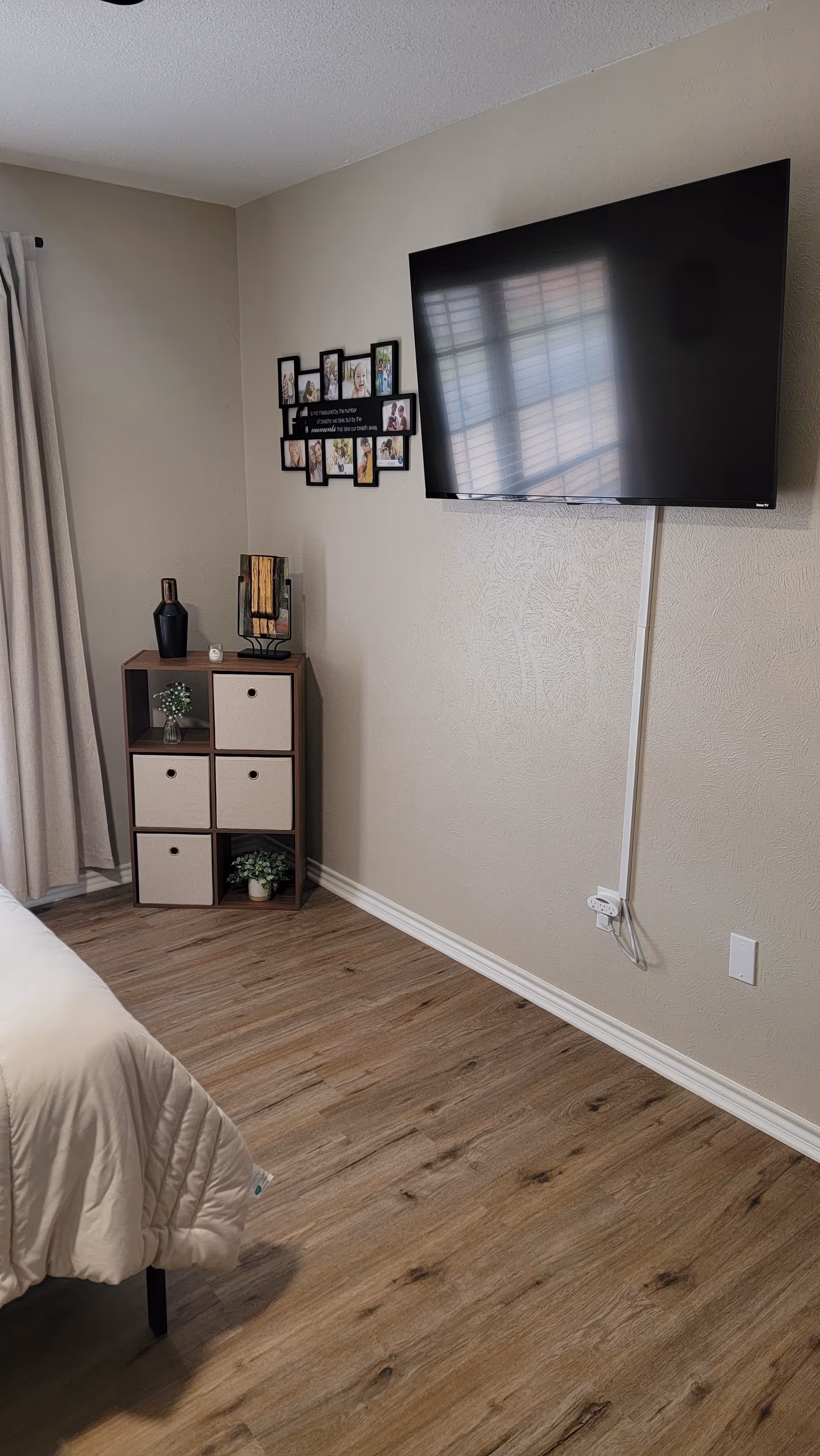 Senior living bedroom with mounted TV, photo collage, and cubby dresser on wood floor
