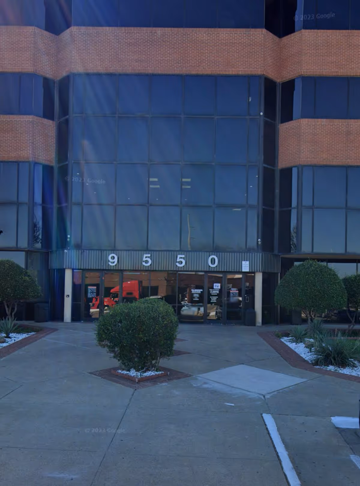 Glass-front building entrance with brick accents and manicured shrubs.