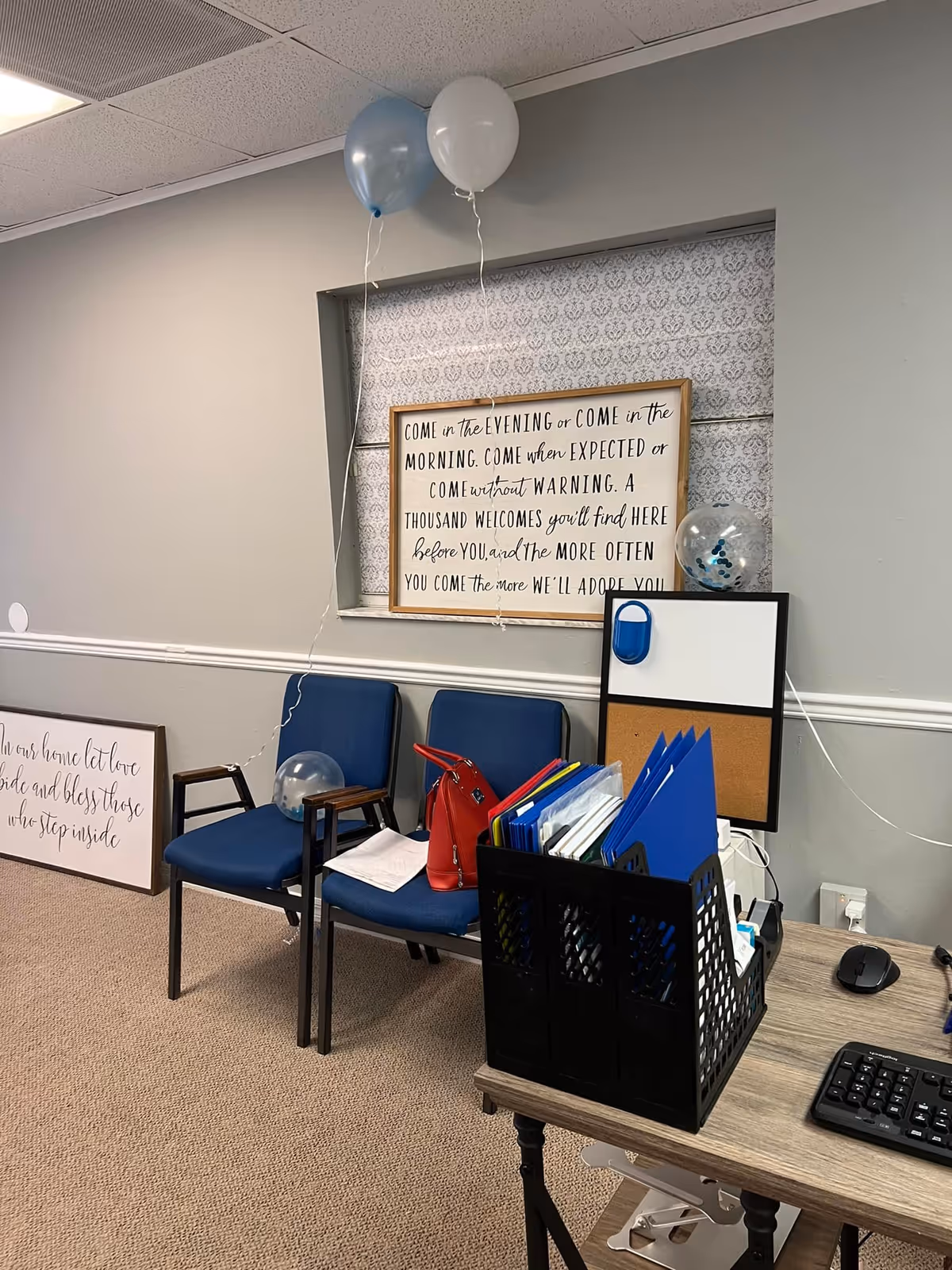 Office desk area in a senior living facility with balloons, blue chairs, and framed quotes.