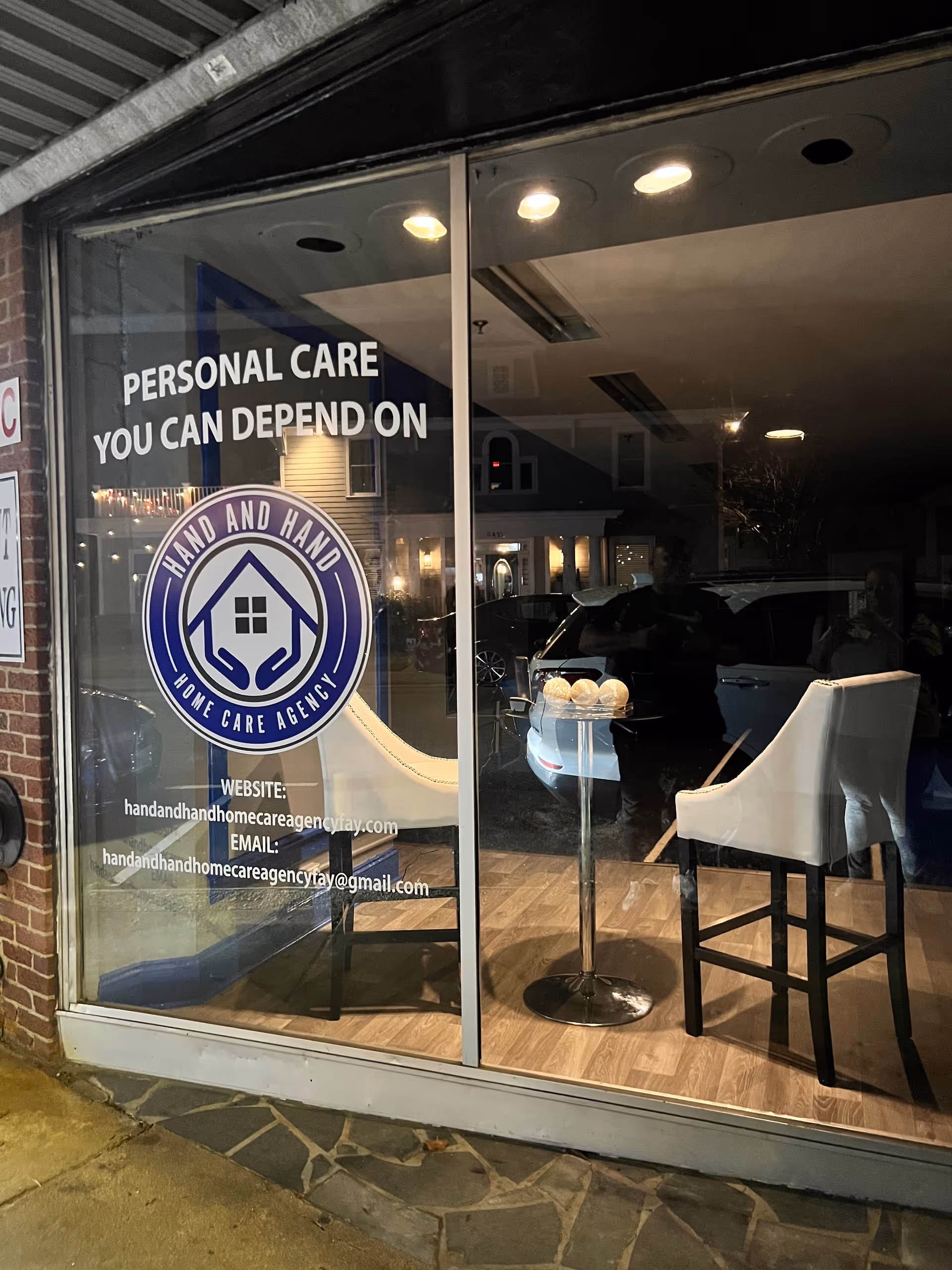 Storefront window for Hand and Hand Home Care Agency with logo and seating inside