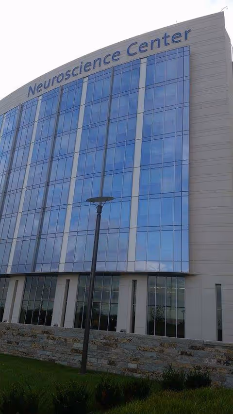 Modern glass-front building labeled Neuroscience Center Infusion Services, seen from ground level.
