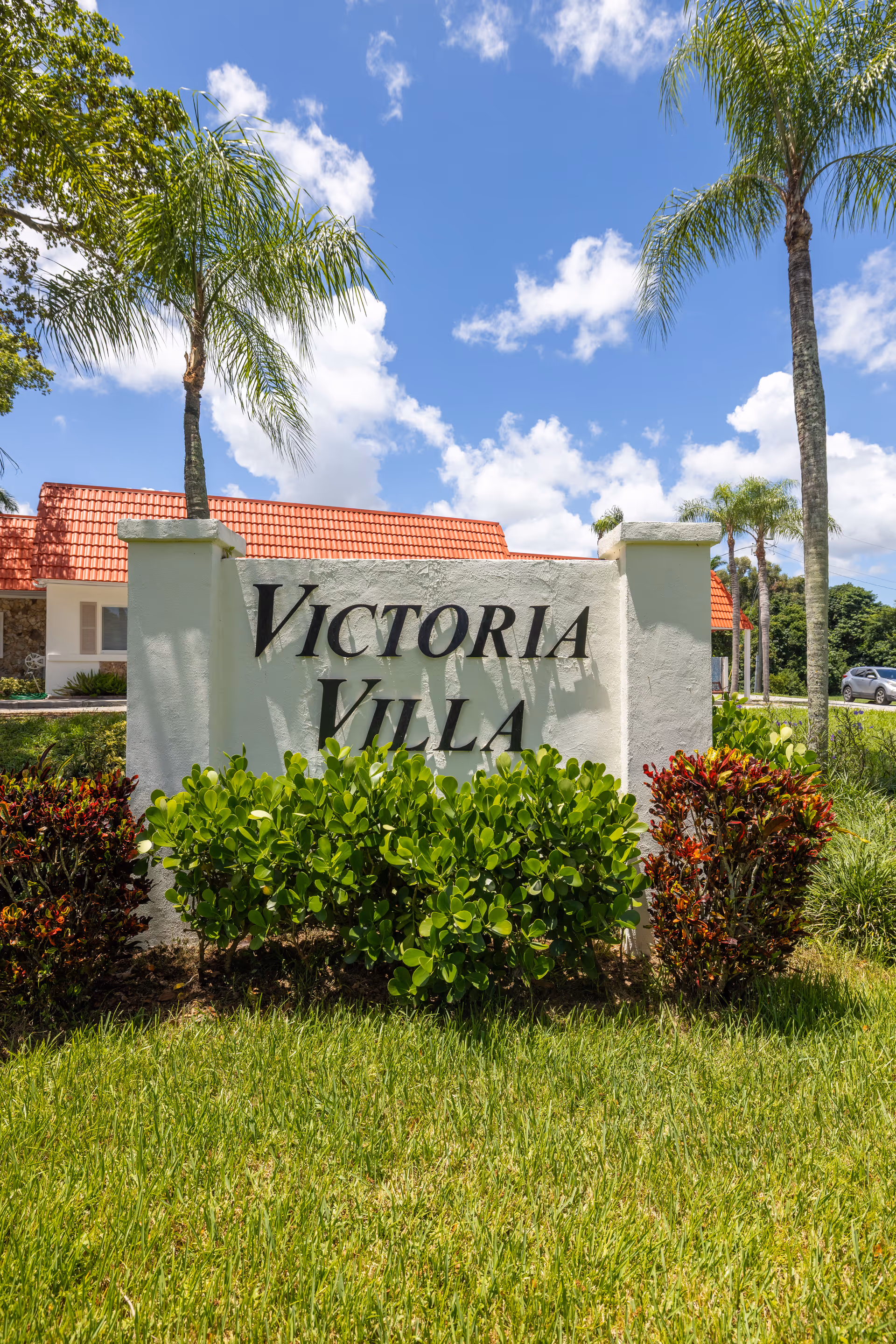 Exterior view of Victoria Villa sign with tropical landscaping and a red-tiled building behind.