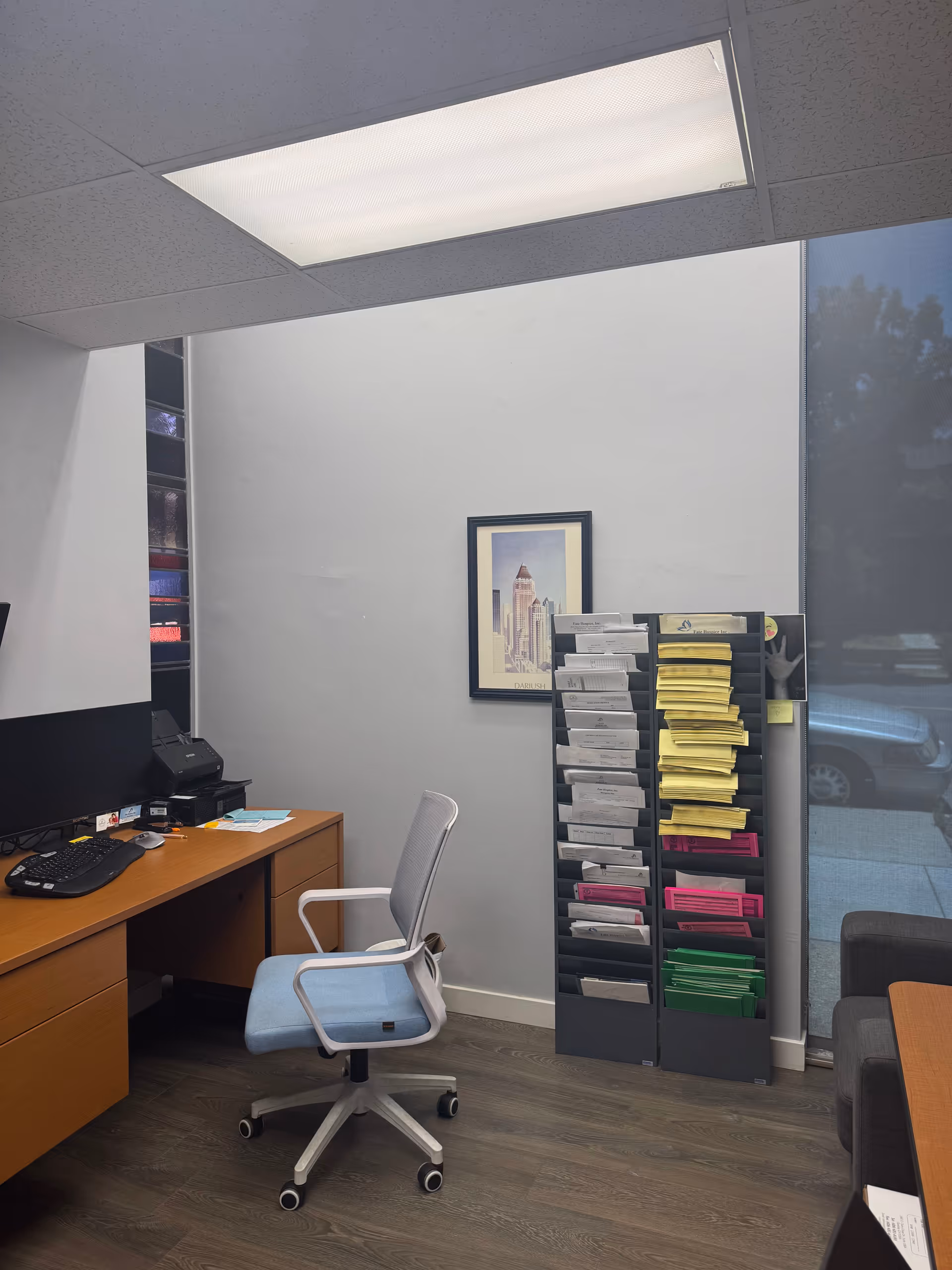 Office workspace with a desk, chair, computer, and a tall file organizer by the wall.