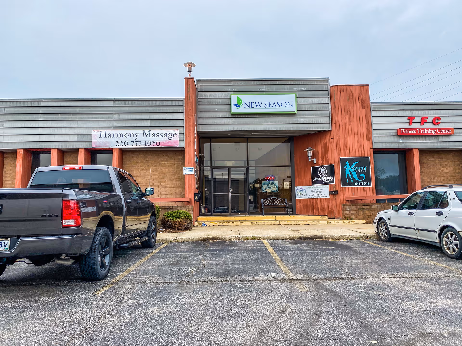 Exterior view of a strip mall storefront with a central glass entrance and parked cars.