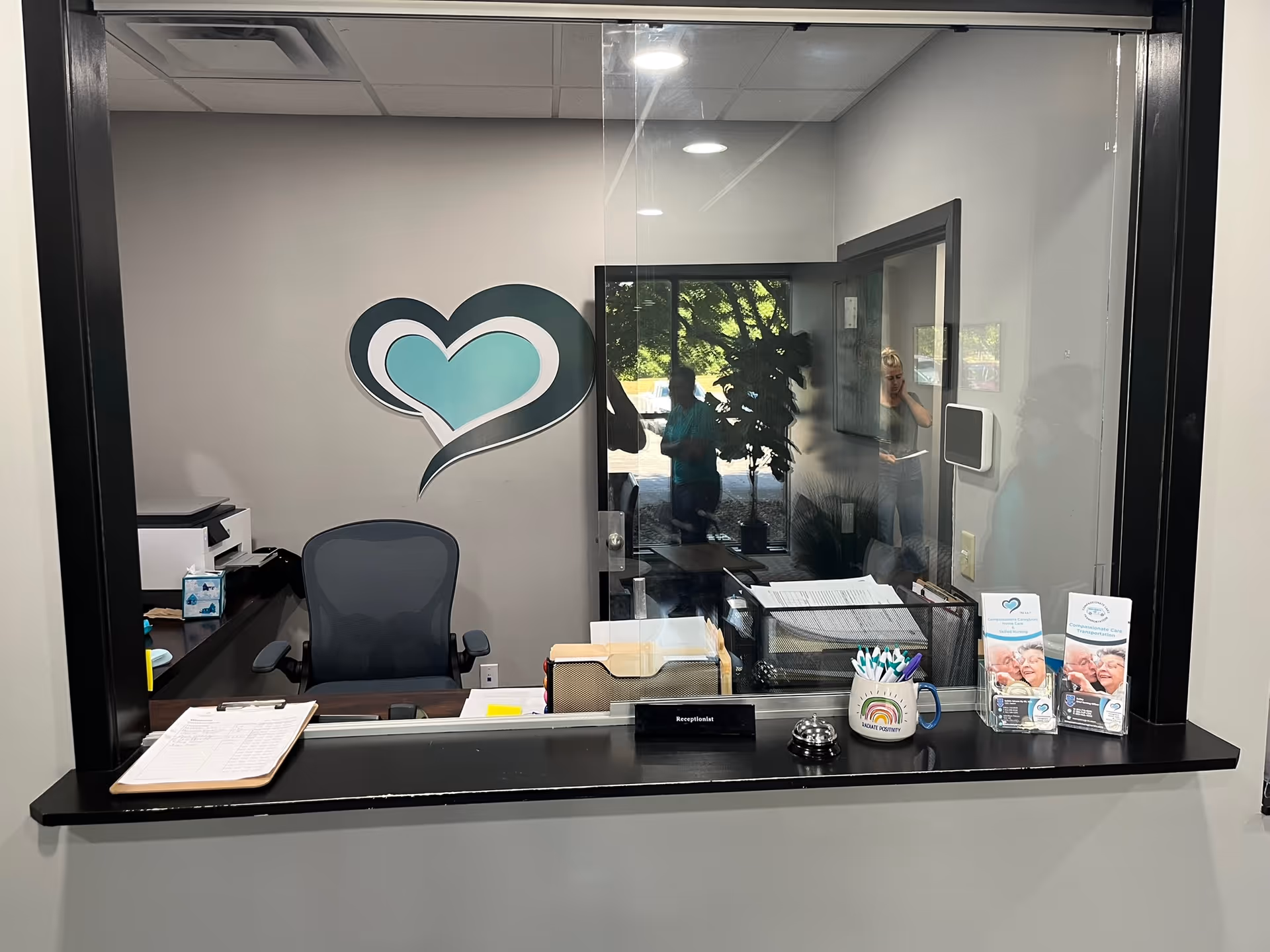 A reception desk inside a compassionate care facility, with a teal heart logo on the wall.