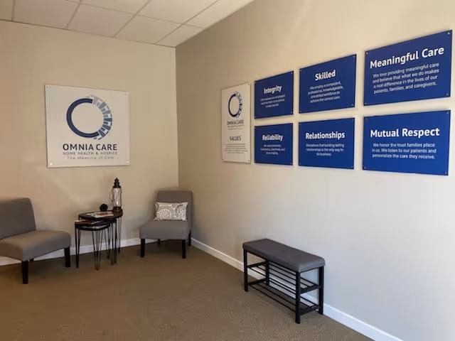 Interior waiting area with Omnia Care logo, blue wall plaques, chairs, and a bench.
