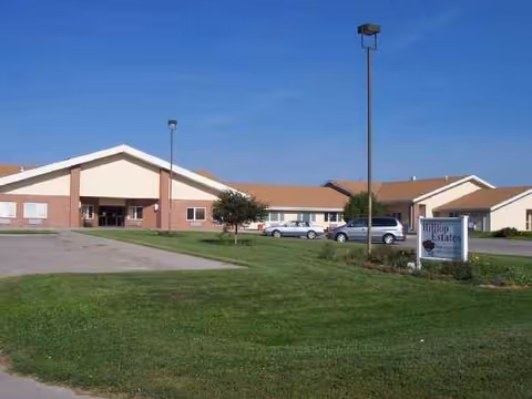 Exterior view of Hilltop Estates senior living facility with parking and a sign.