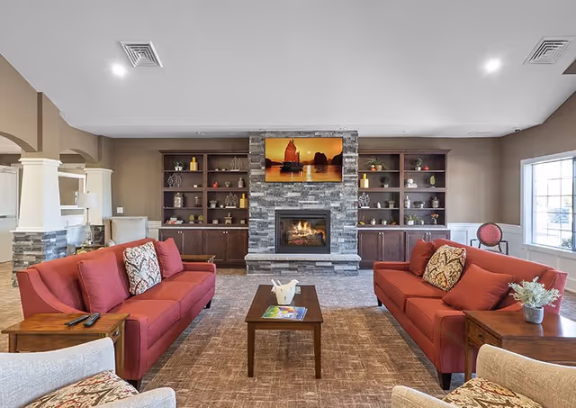 Cozy lounge with red sofas surrounding a central coffee table, stone fireplace, and built-in shelves.
