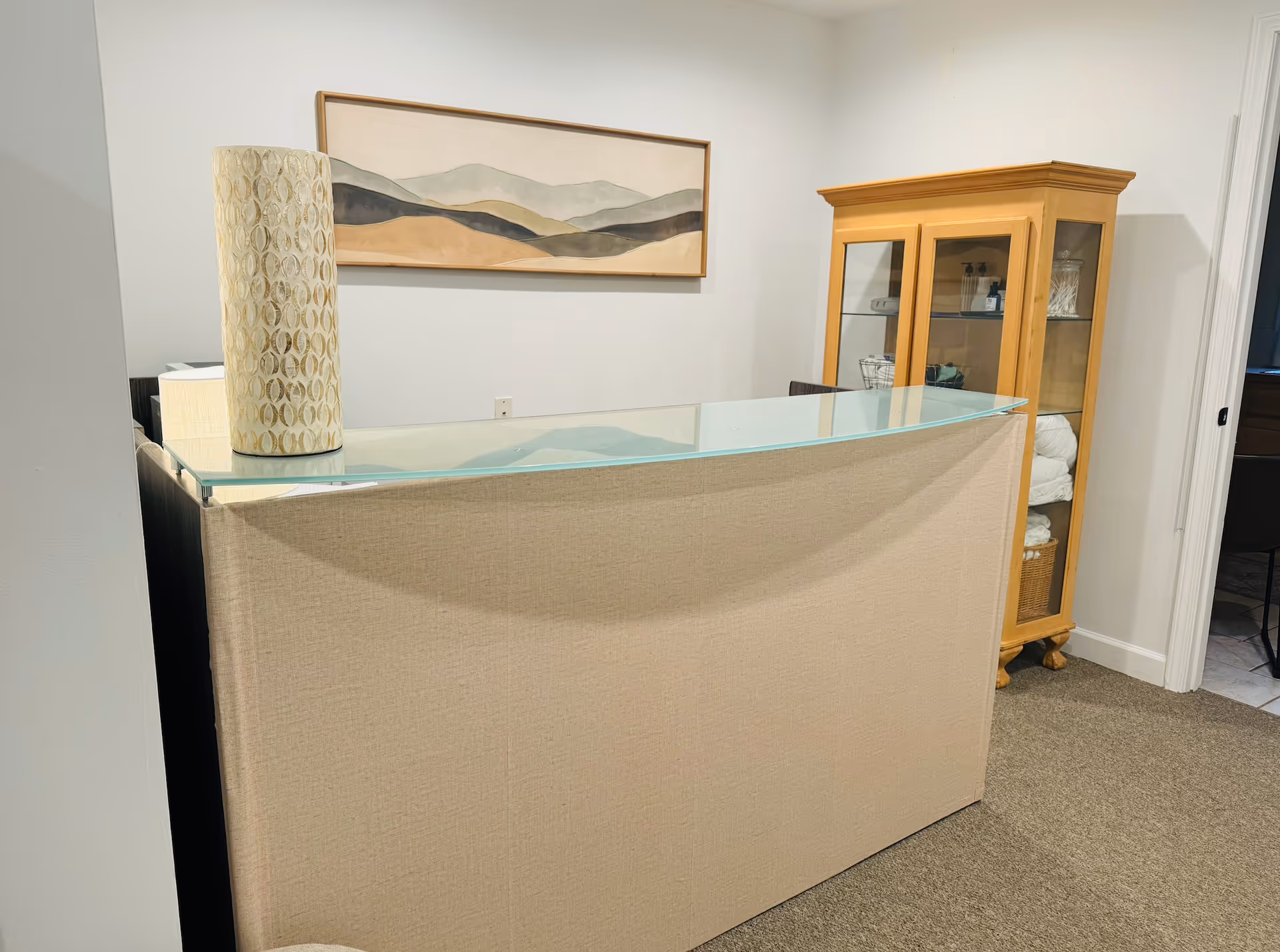 Reception area with glass-topped desk, artwork, and cabinet in a neutral senior living lobby.