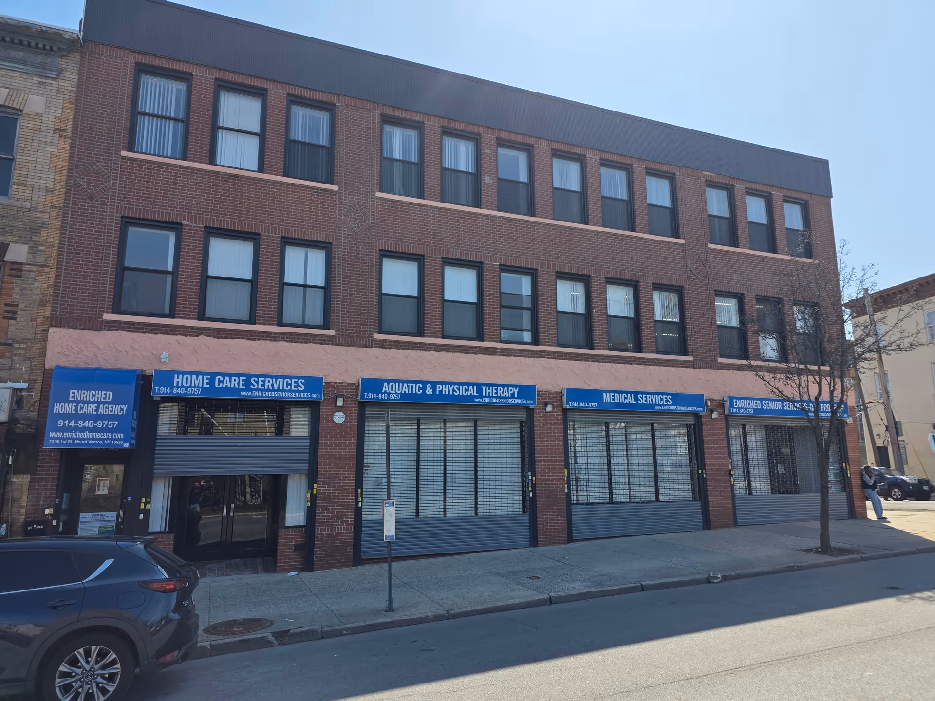 Brick three-story building with storefronts and blue signs along the street.