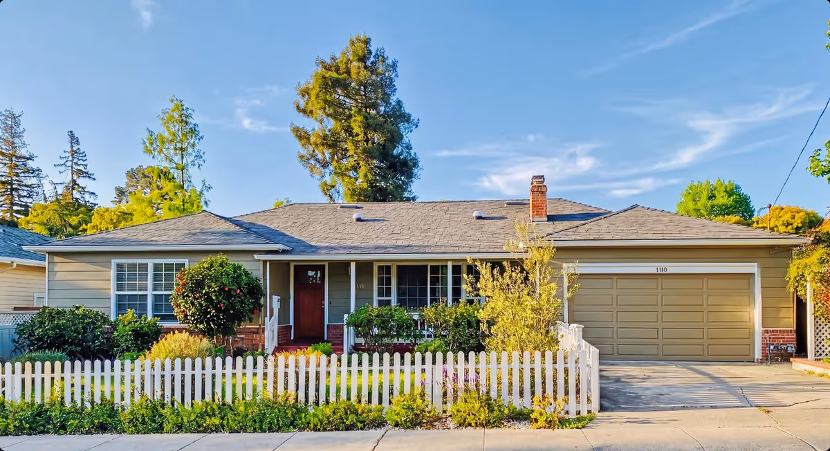 A single-story senior living facility with a white picket fence and manicured front garden.