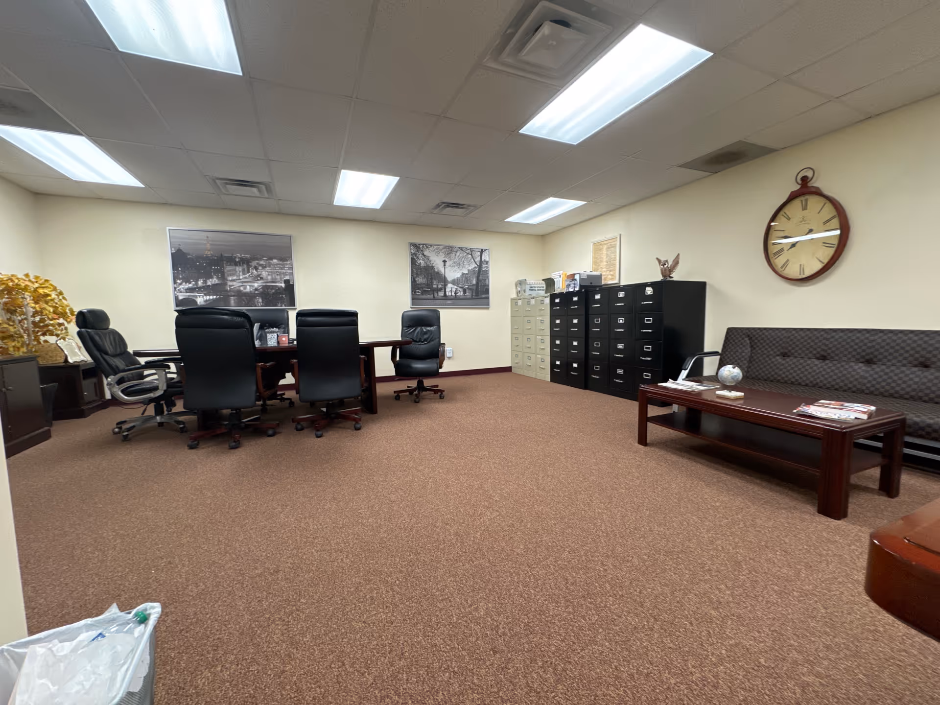 Office conference area with a long table, black chairs, filing cabinets, and a couch.