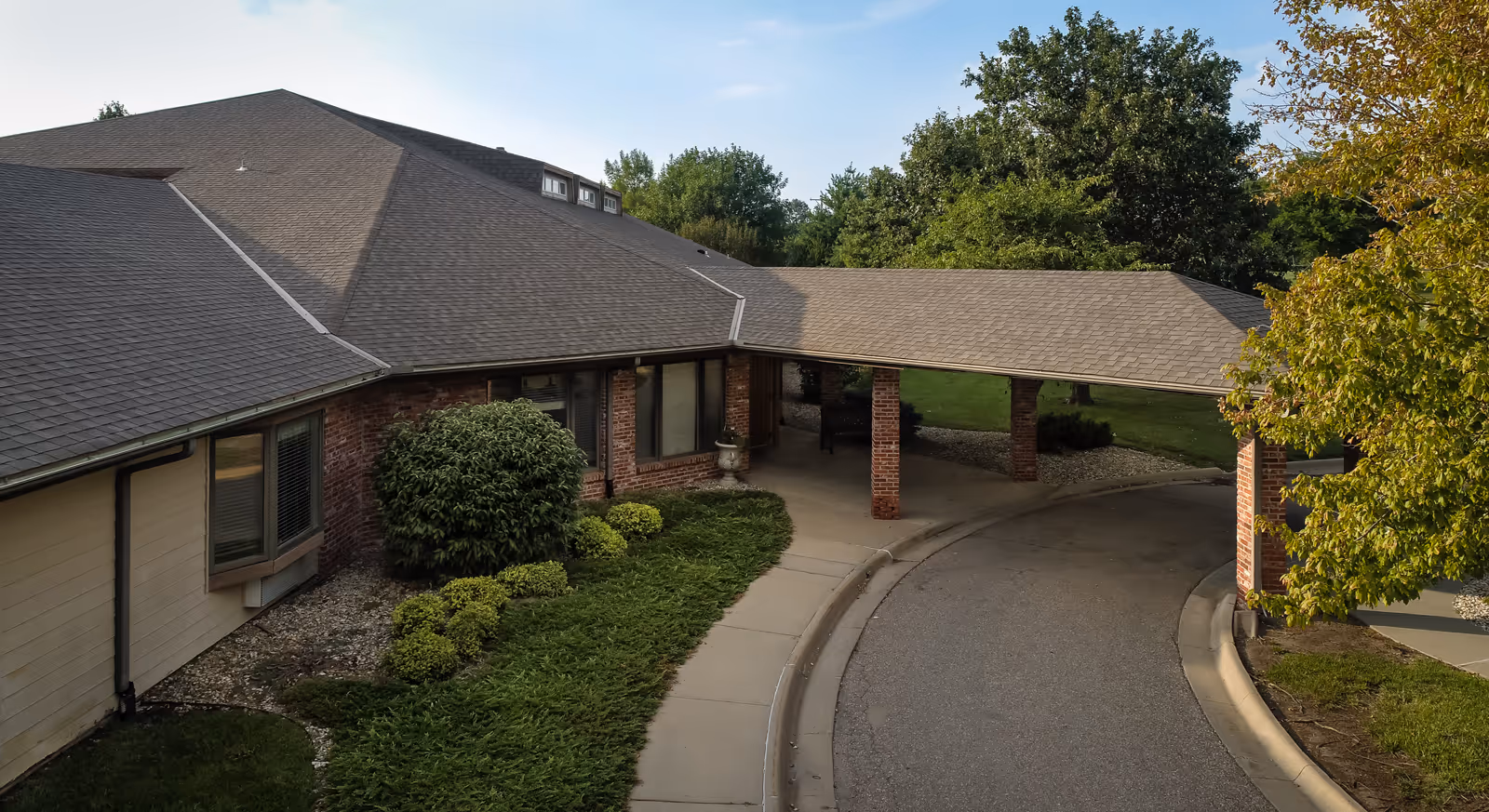 Front exterior of a single-story brick assisted living building with a covered drive-through entrance and surrounding landscaping.