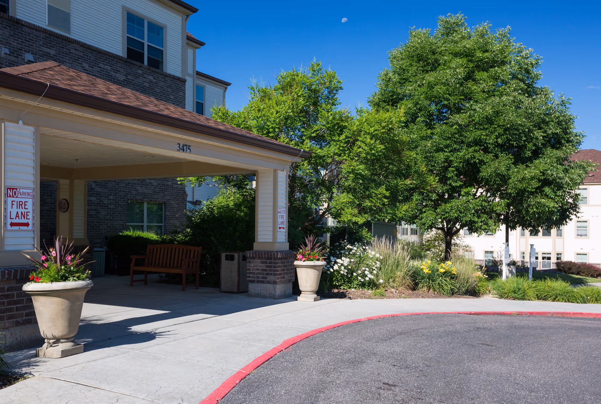 Exterior view of The Belcaro entrance with a covered drop off, brick columns, benches, and landscaping.